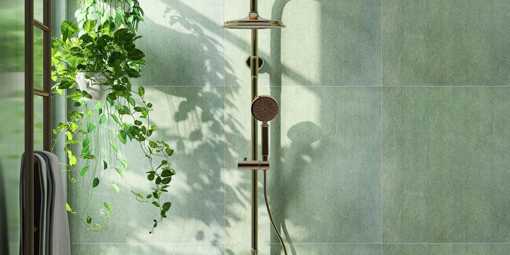 Modern and luxury bathroom design with shiny gold colored rain shower, shower head on slide bar on beautiful green granite wall and creeper plant with sunlight from window for home interior decoration, architecture and design background.