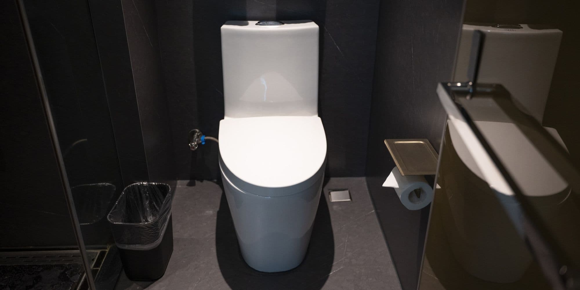 A sleek, modern bathroom featuring a white toilet and mirror, set against dark walls for contrast. The space is compact yet stylish, suitable for contemporary home or office settings.
