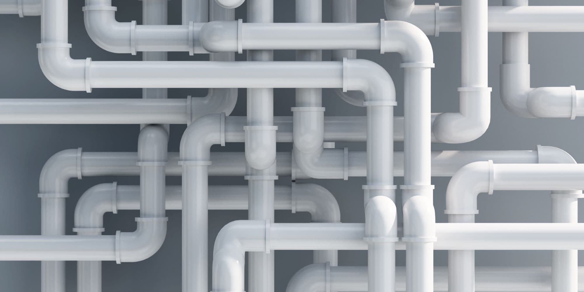 A close view of various white plumbing pipes intersecting and intertwining against a simple gray background.